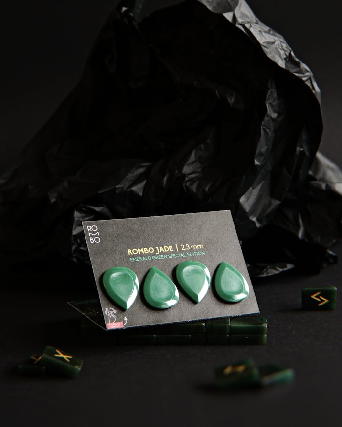 Close-up of emerald green guitar picks against a black foil background, featuring a close inspection of the special edition design.